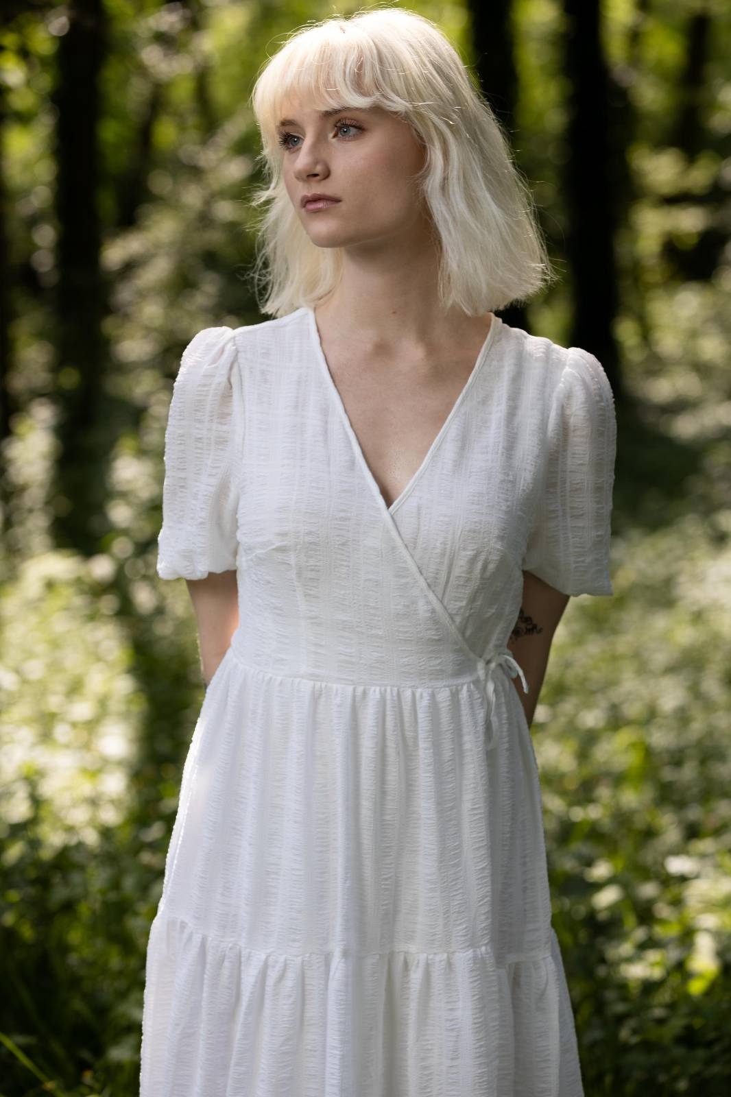 blondes weibliches Model mit langem weißen Kleid in heller Waldlandschaft