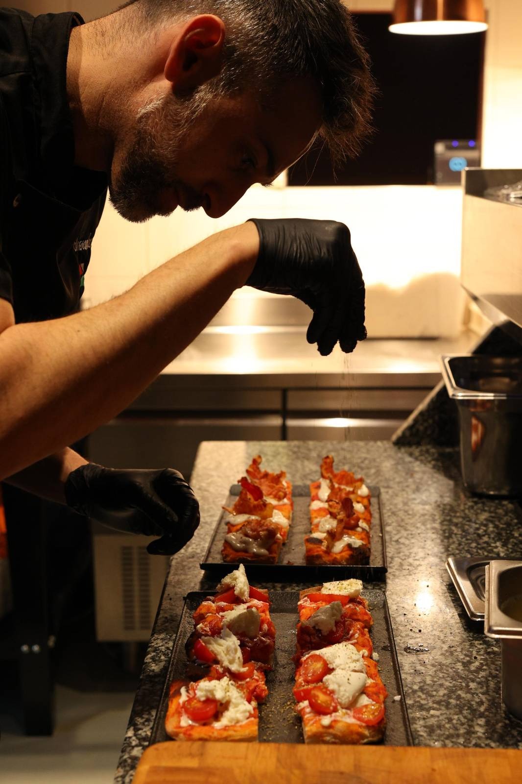 male chef sprinkling salt over fresh pizza slices