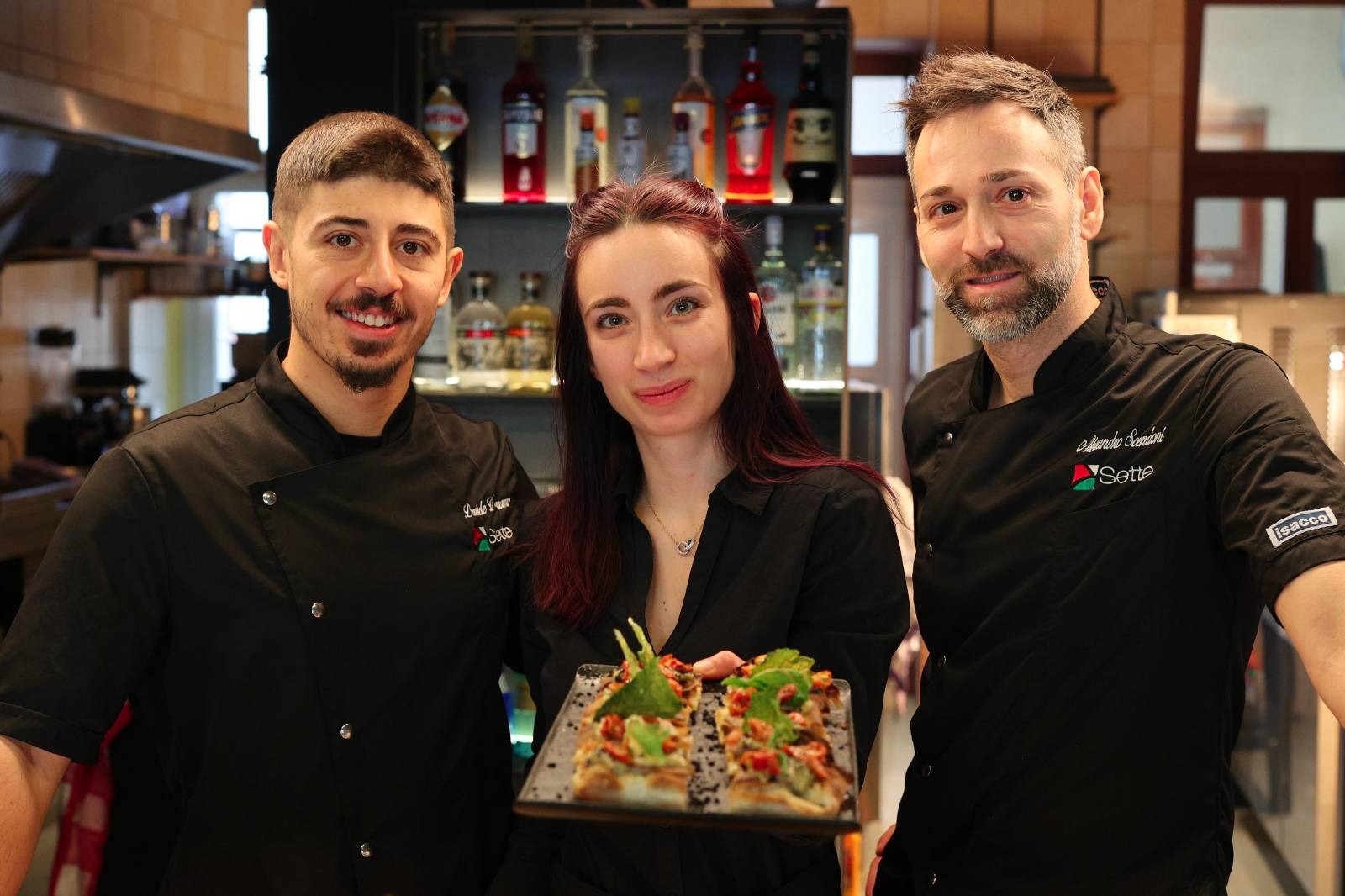 kitchen team standing in front of bar with plate of small pizza slices