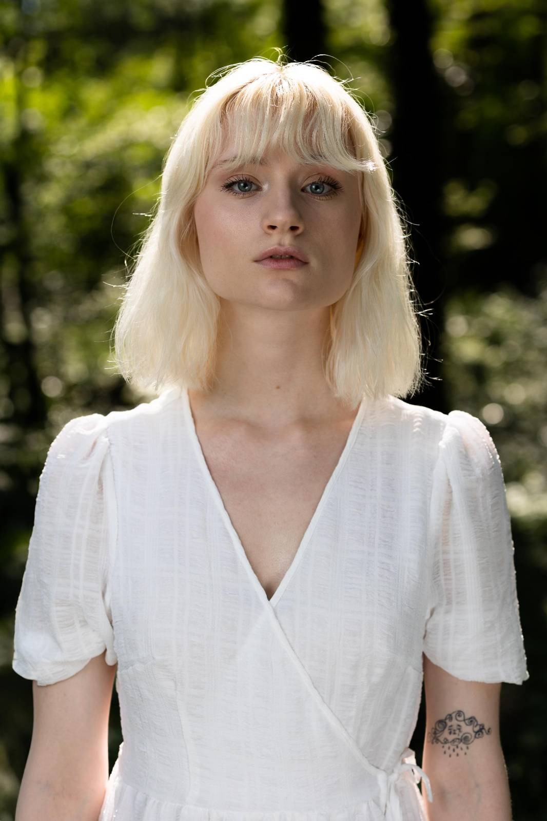 blondes weibliches Model in weißem Kleid in grüner Waldlandschaft